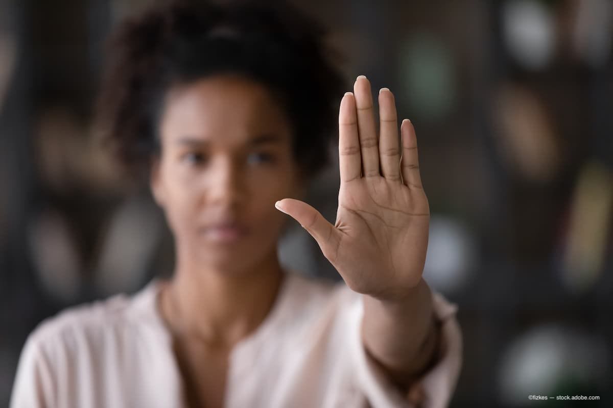 a woman holding up her hand in front of the camera signifying stop. (Image Credit: AdobeStock/fizkes)