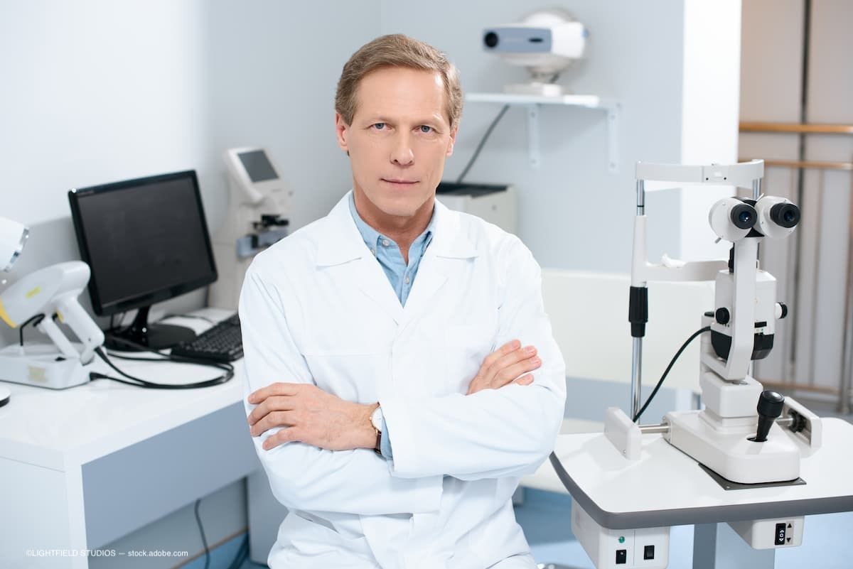 ophthalmologist sitting with crossed arms near slit lamp in consulting room. (Image Credit: AdobeStock/LIGHTFIELD STUDIOS)