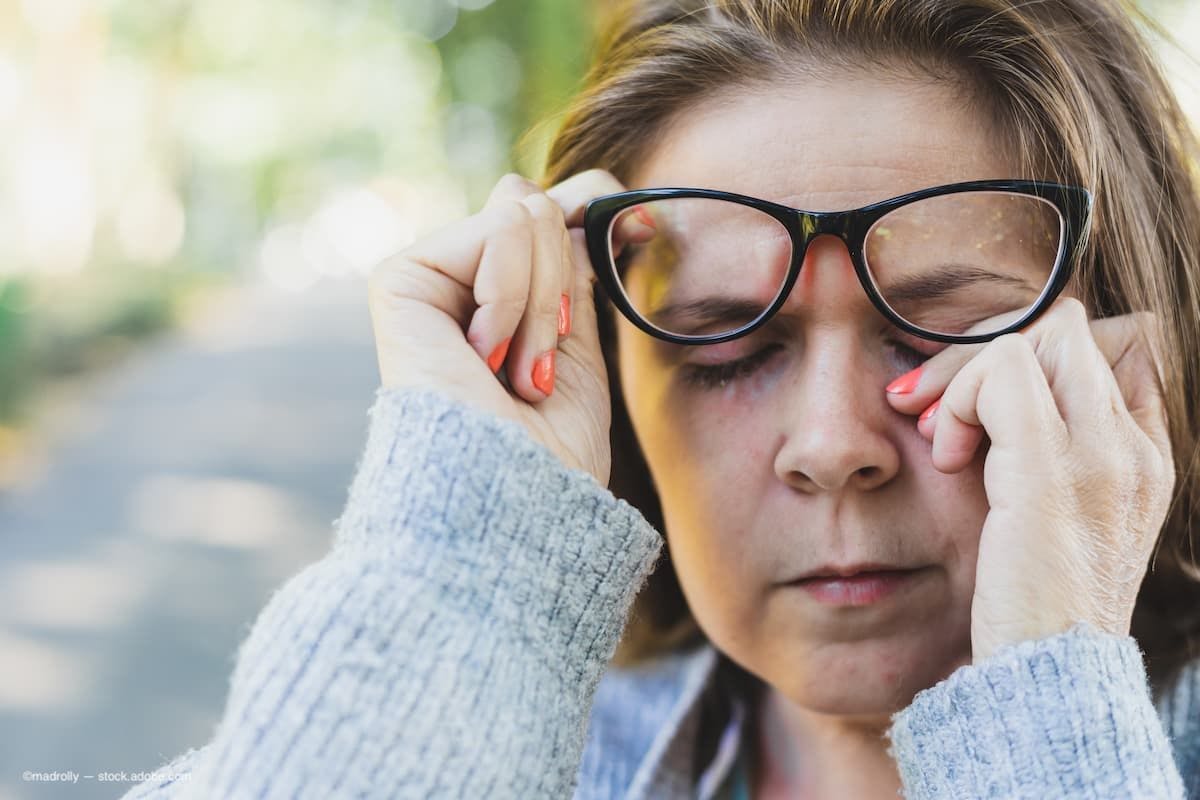 a woman holding her glasses up and rubbing her eyes while outside. (Image Credit: AdobeStock/madrolly)