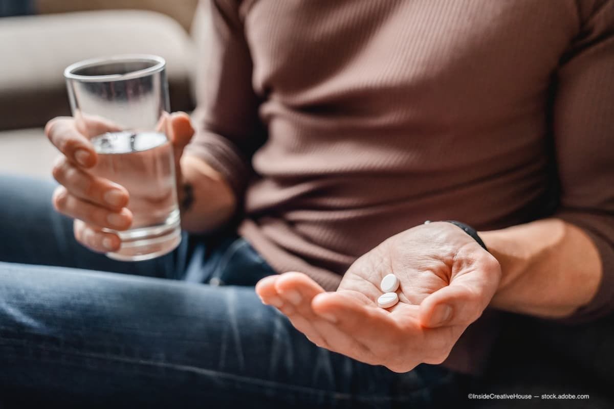 An older man holding a glass of water in one hand and pills in the other. (Image Credit: Adobe Stock/InsideCreativeHouse)