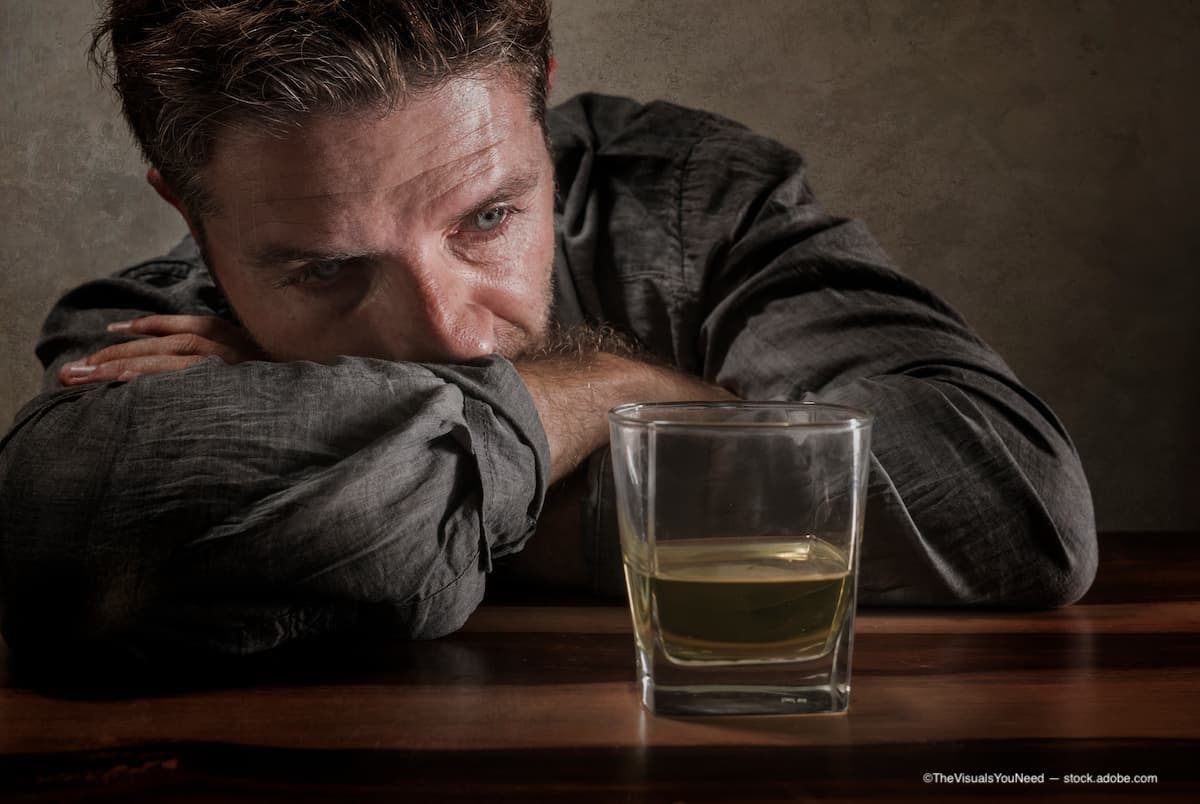 A desperate man addicted to alcohol who is looking at a glass full of whisky. (Image Credit: AdobeStock/TheVisualsYouNeed)