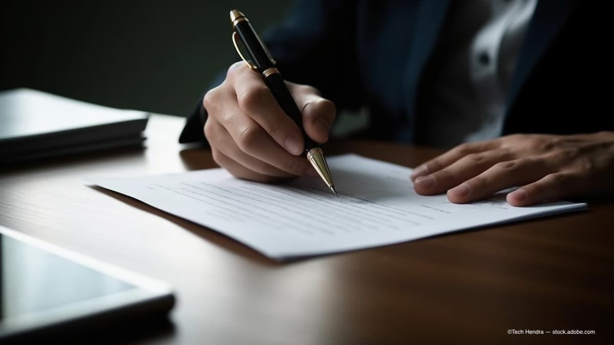 a man sitting at a table signing a contract. (Image Credit: AdobeStock/Tech Hendra)