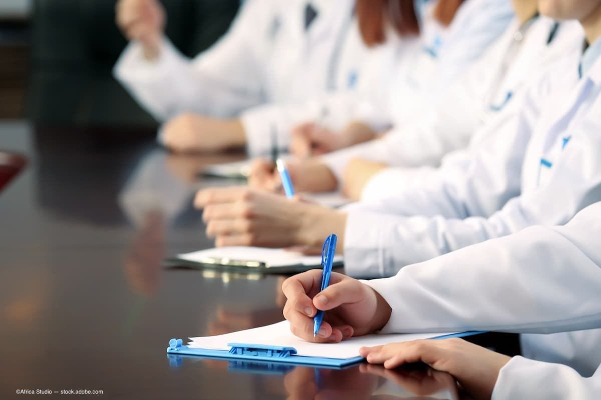 A group of doctors sitting at a table and writing on clipboards. (Image Credit: AdobeStock/Africa Studio)