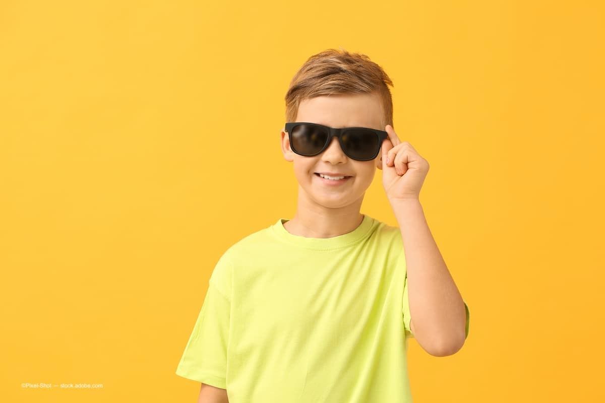 a child in yellow wearing sunglasses and smiling. (Image Credit: AdobeStock/Pixel-Shot)